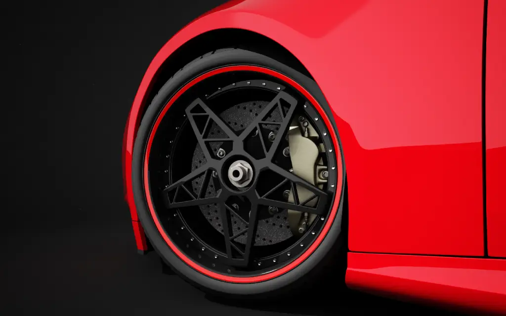 Close-up of a red sports car's rear wheel with a black, multi-spoke rim accented by a red trim. Large disc brake and caliper are visible behind the rim. The car body is sleek and glossy under dramatic lighting.