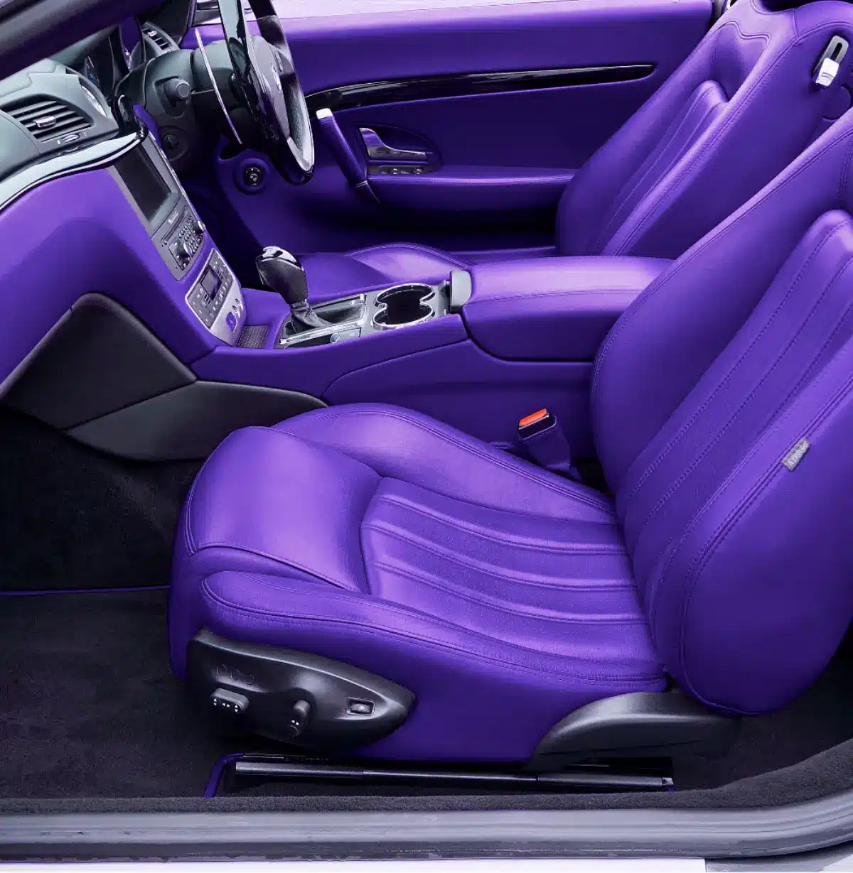 The interior of a car featuring vibrant purple leather seats and purple accents on the doors and dashboard. The steering wheel, center console, and controls are also visible. The interior of a car featuring vibrant purple leather seats and purple accents on the doors and dashboard. The steering wheel, center console, and controls are also visible.