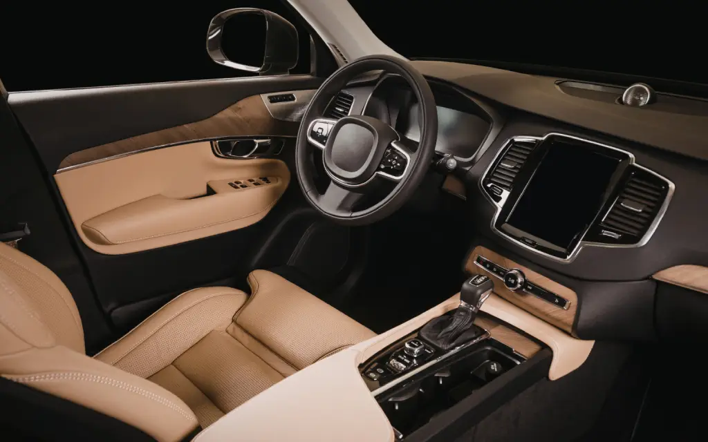 Modern car interior featuring beige leather seats, a multifunctional steering wheel, a digital display on the dashboard, and wood-grain accents on the doors and console.