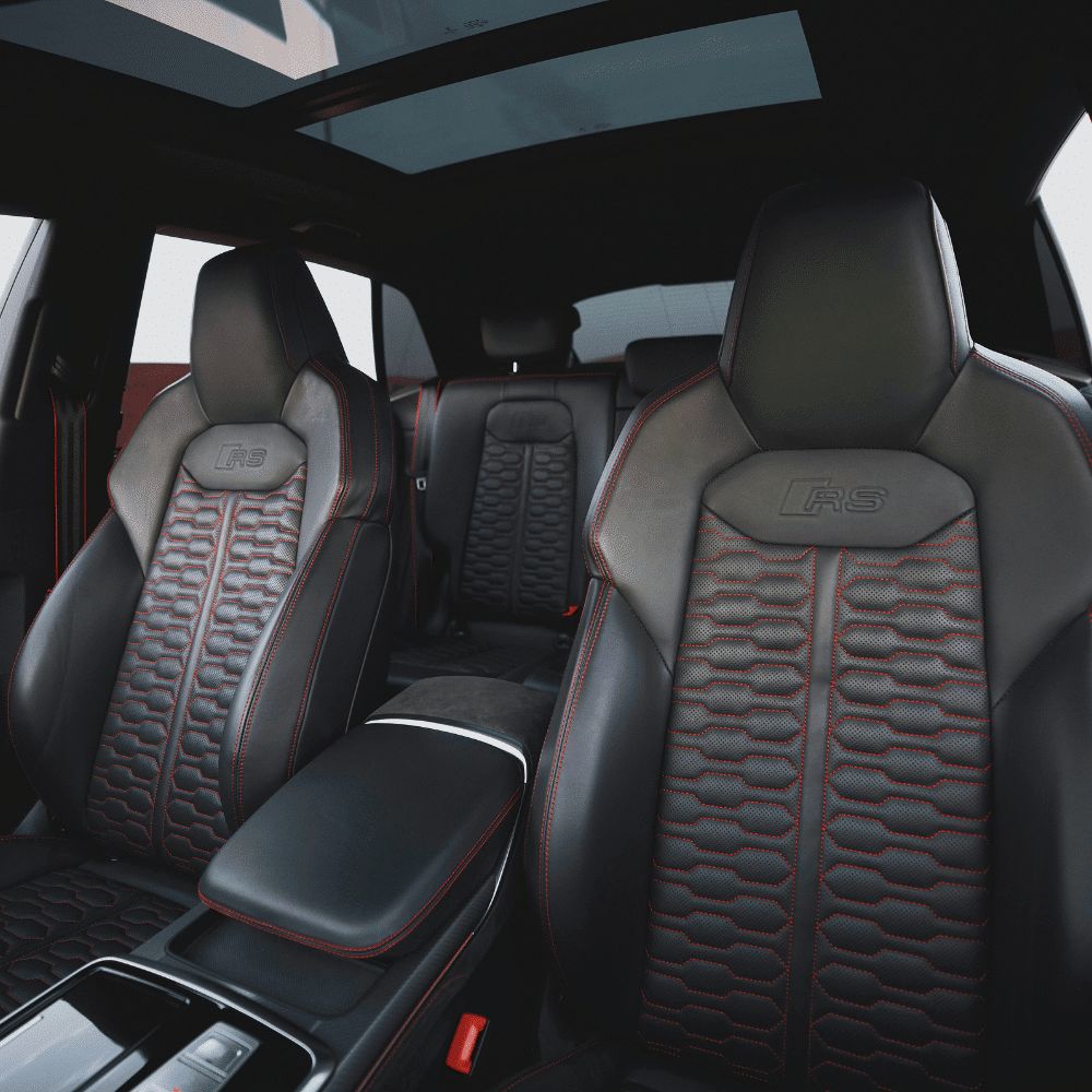 The interior of a luxury car featuring black leather seats with red stitching, “RS” embossed on the front seats, a panoramic sunroof, and modern center console. The back seats have similar detailing.