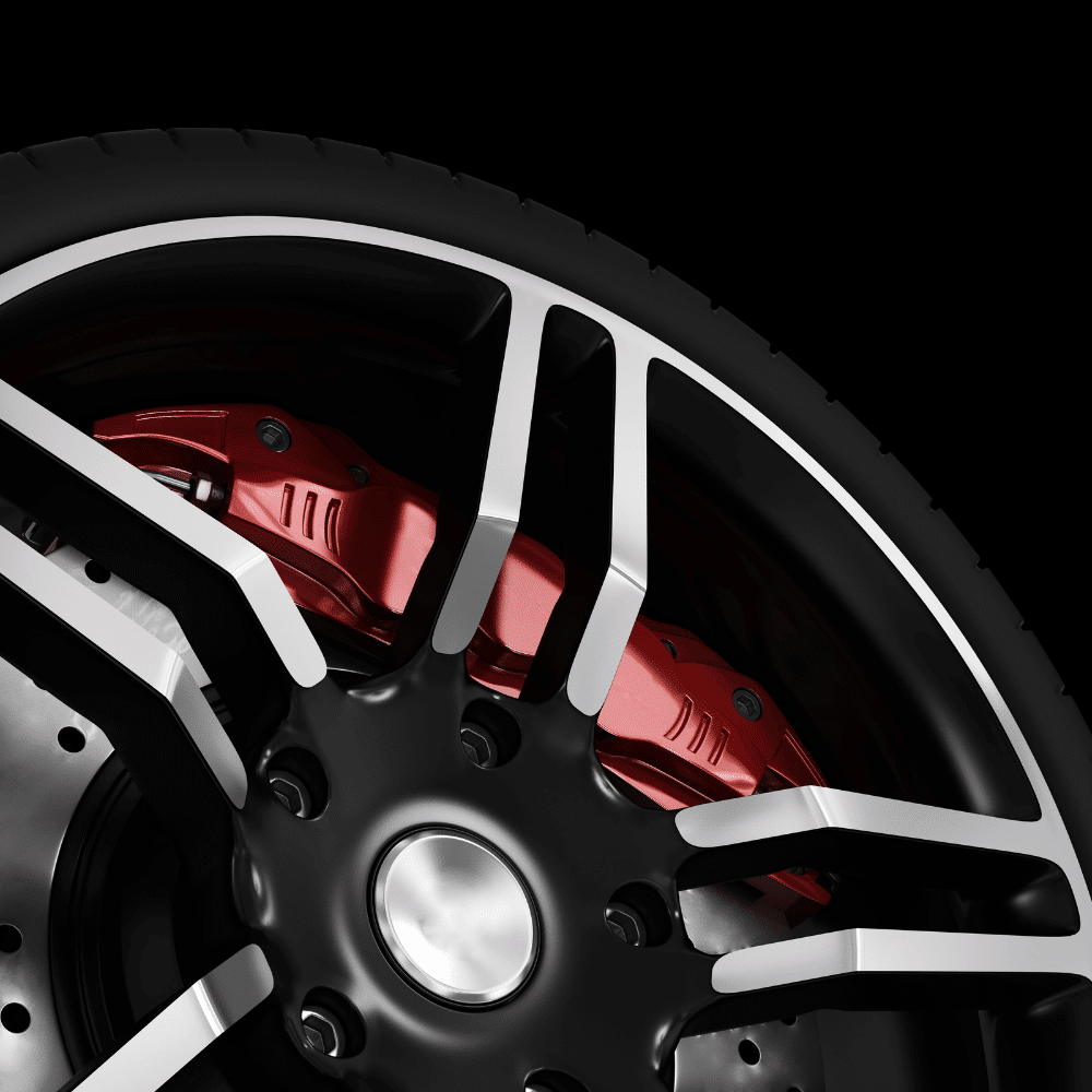 Close-up of a black and silver car wheel with a red brake caliper and a ventilated brake disc, set against a black background. The metallic spokes and tire tread details are clearly visible.